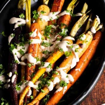 Roasted carrots with creamy tahini sauce and herbs in a black dish.