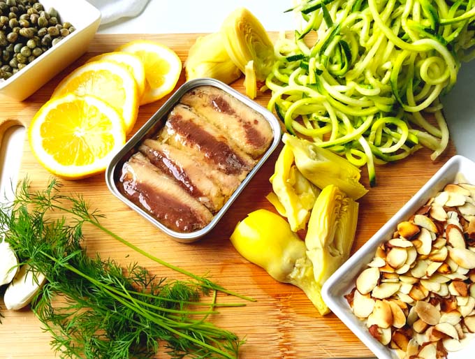 Sardines in open tin on wood cutting board with zucchini lemon dill almonds