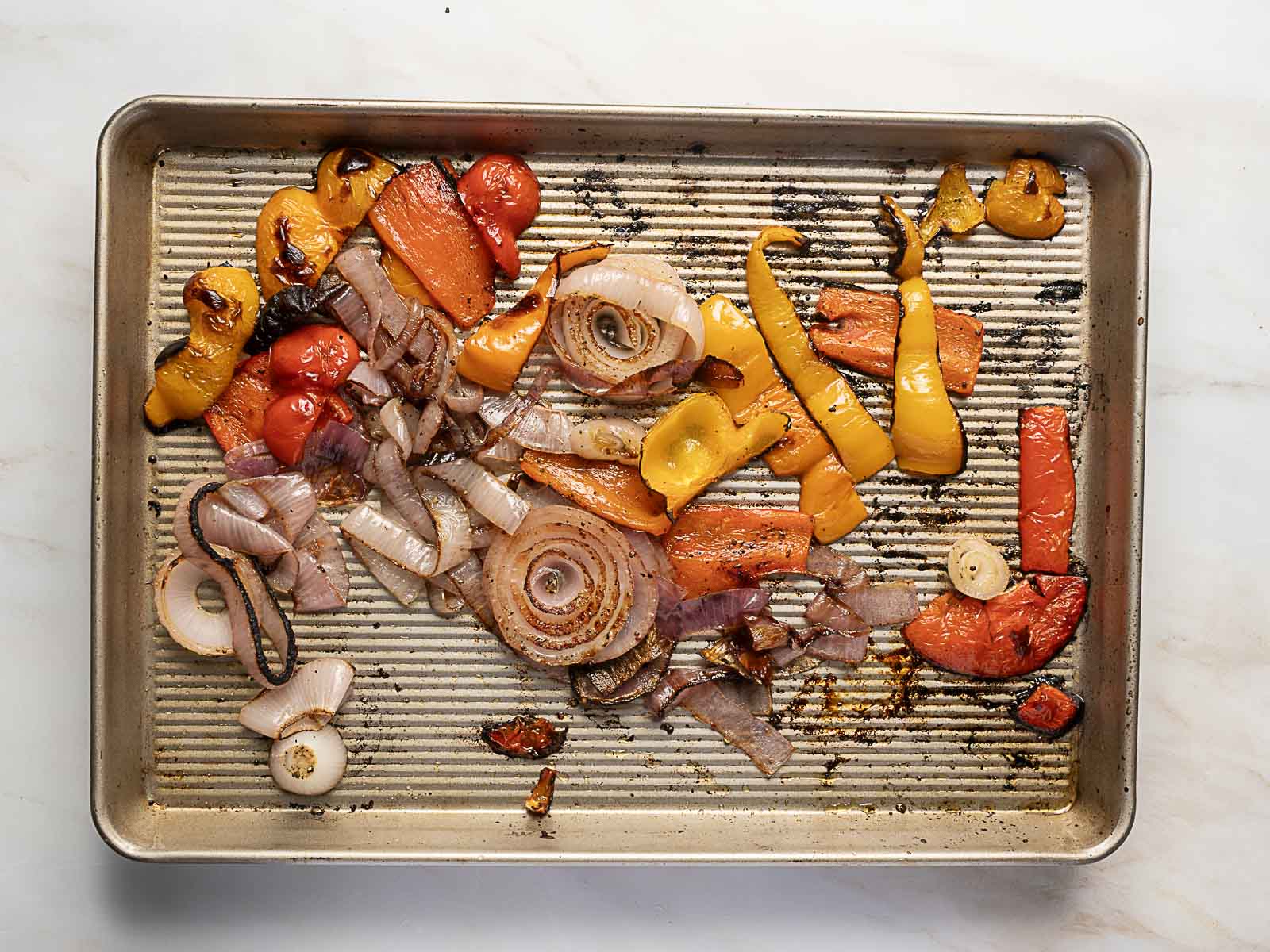 A baking sheet with assorted roasted vegetables, including sliced onions, bell peppers, tomatoes, and carrots-perfect for adding to a vibrant Rainbow Potato Salad.
