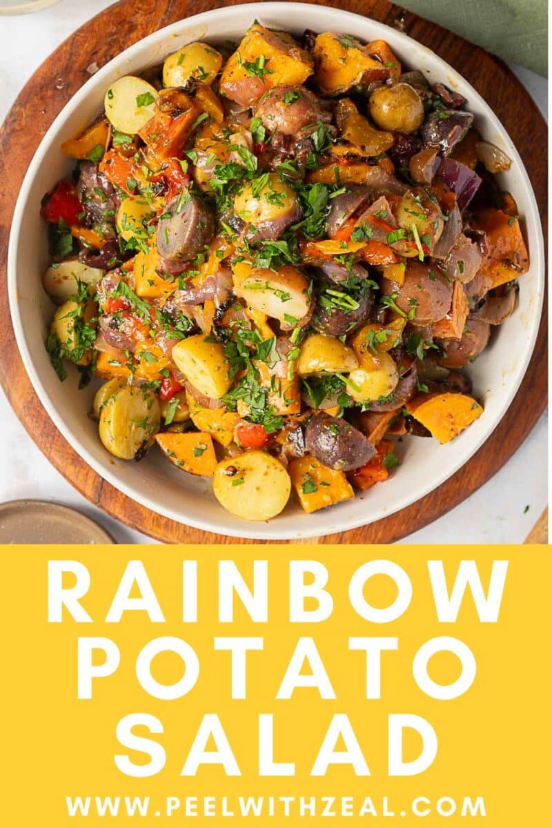 A vibrant bowl of Rainbow Potato Salad with fresh chopped herbs on top, set on a wooden board.