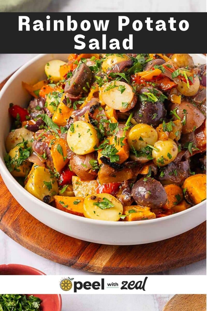 A bowl of Rainbow Potato Salad with colorful potatoes, fresh herbs, and crisp vegetables sits on a wooden surface.