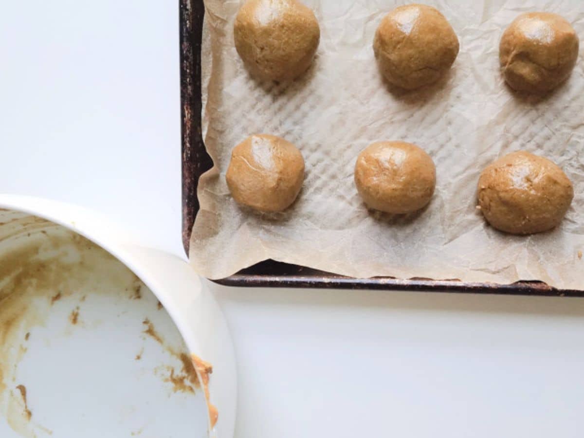 Six buckeyes protein balls rest on a parchment-lined baking tray, joined by an empty mixing bowl with remnants.