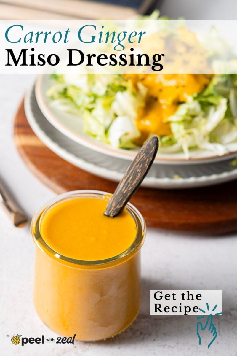 A jar of carrot ginger dressing with a wooden spoon is in the foreground, while a plate of salad drizzled with the same dressing sits in the background. Text reads “Carrot Ginger Miso Dressing. Get the Recipe.”.