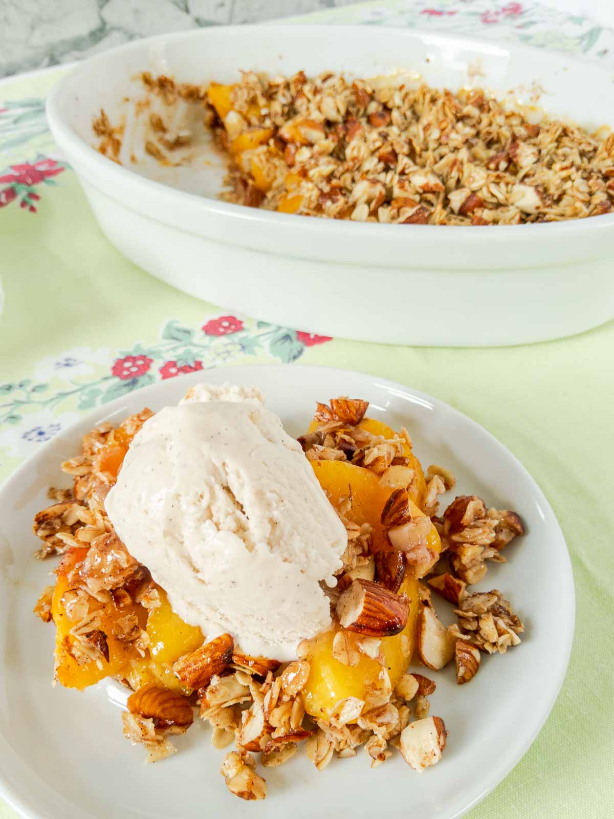 serving of peach crisp with baking dish in background