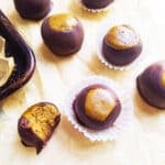 Protein peanut butter and chocolate buckeyes rest on parchment paper, with one partially eaten to reveal a creamy peanut butter center.
