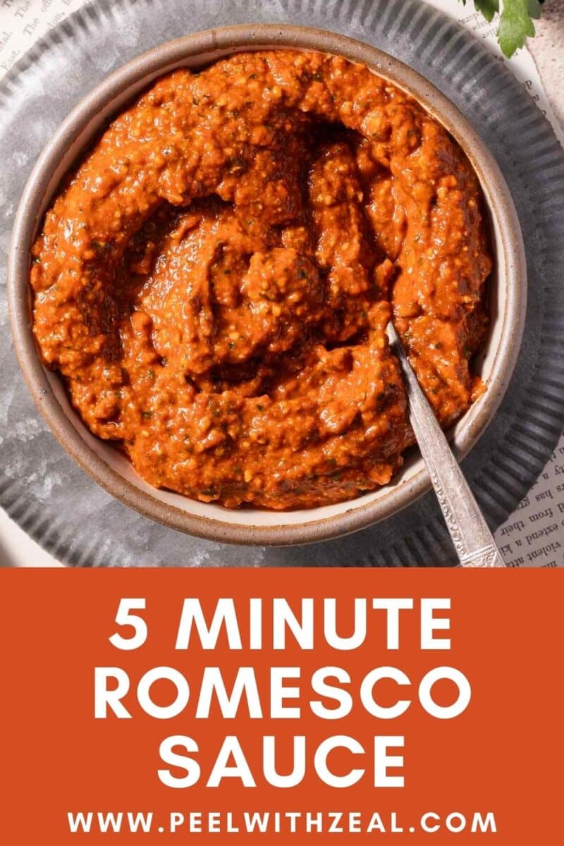 A bowl of no-cook Romesco sauce with a spoon, set on a gray plate. Text below reads: "5 Minute No-Cook Romesco Sauce, www.peelwithzeal.com.
