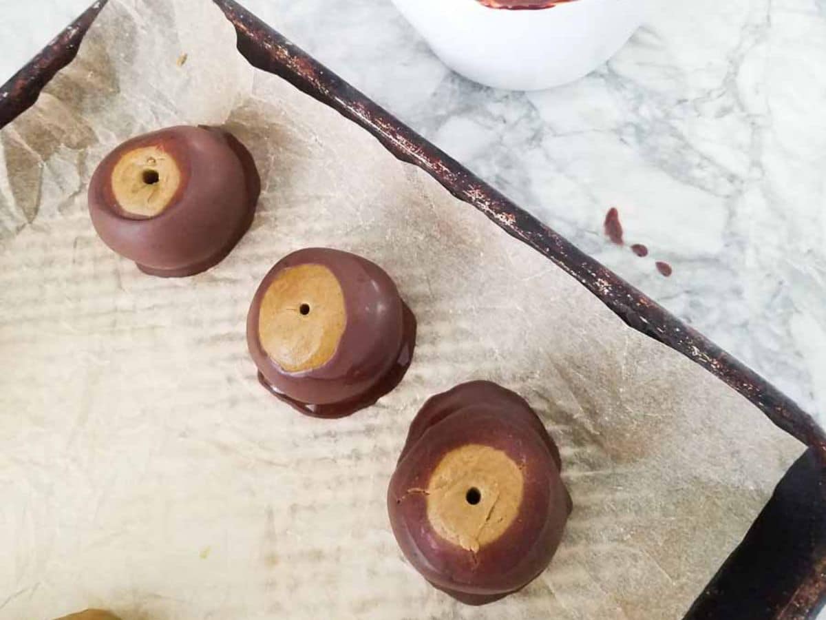 Three protein balls rest on parchment paper, partially coated in rich chocolate, with a bowl in the background.