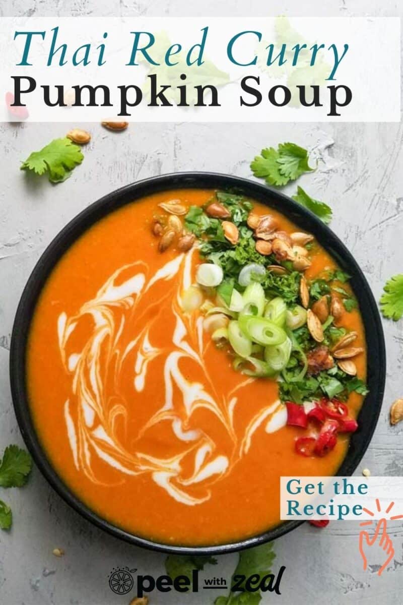 A bowl of Thai pumpkin soup brimming with red curry flavors, garnished with cilantro, green onions, sliced chili, and pumpkin seeds. Creamy swirls dance on the surface of this vibrant dish.