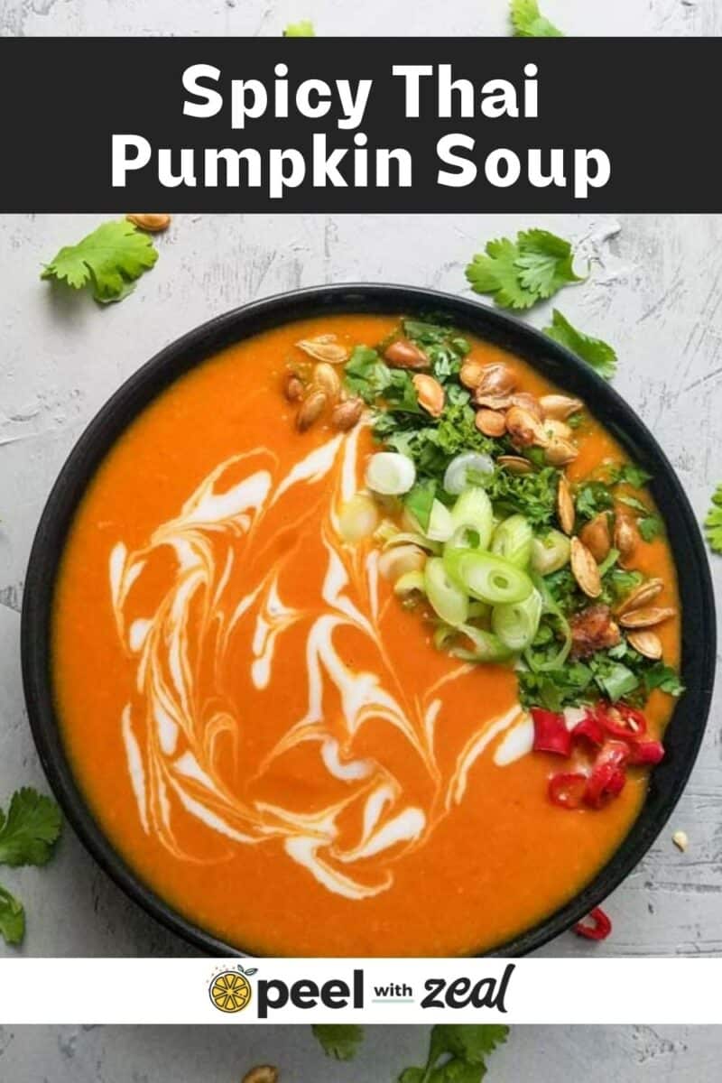 A bowl of Thai pumpkin soup with a spicy swirl pattern, garnished beautifully with scallions, red chili, pumpkin seeds, and cilantro.