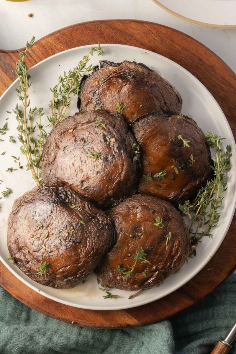 A plate of four roasted portobellos garnished with sprigs of thyme.