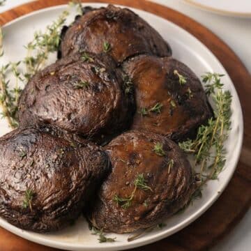 A plate of roasted portobello mushrooms garnished with sprigs of fresh thyme.