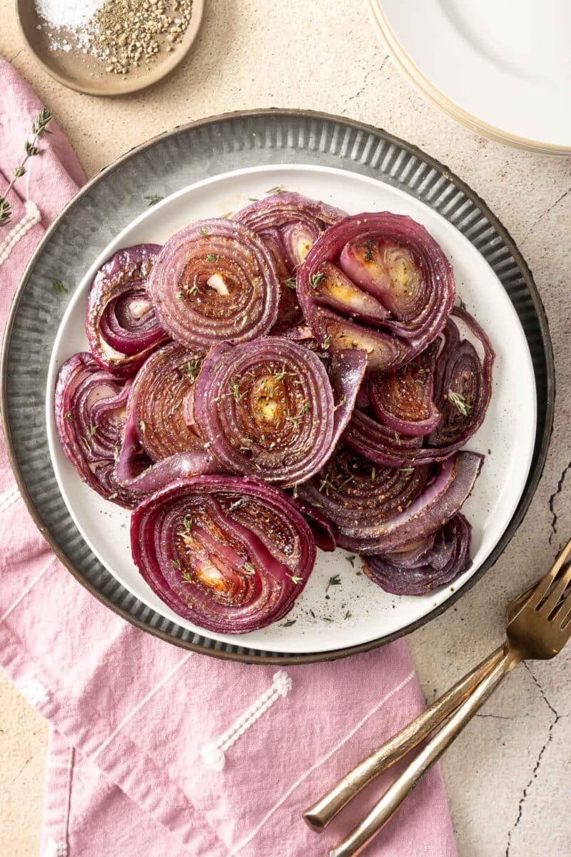 A plate of roasted red onion slices garnished with fresh herbs sits invitingly on the table, accompanied by a pink napkin and a fork.