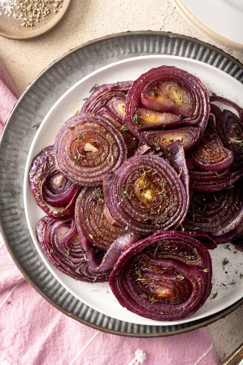 A plate of roasted red onions garnished with herbs and spices rests elegantly on a pink napkin.