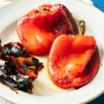 Two beautifully roasted peppers rest on a plate, their charred skin pieces scattered beside them.