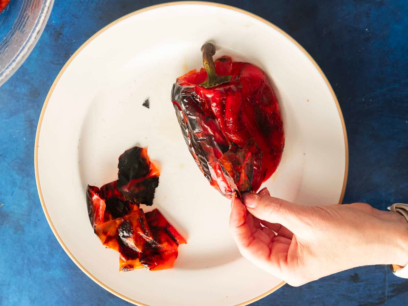 Carefully hand peeling the charred skin off roasted red peppers on a pristine white plate, revealing their vibrant hue beneath.