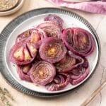 A beautifully arranged plate of roasted red onions, perfectly seasoned with herbs, sits invitingly on a white and black rimmed plate.