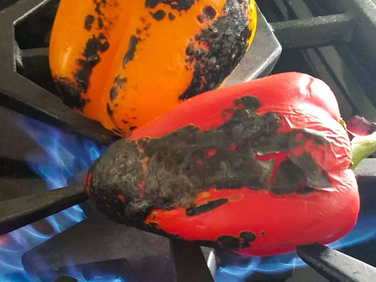 Two vibrant bell peppers, one red and one orange, sizzle as they transform into perfectly roasted peppers over the open flame on a stove.