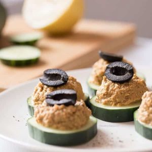sliced cucumber rounds with sardine dip olives on white plate.
