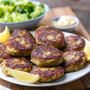 brown and crispy fish cakes on white plate with lemon wedges