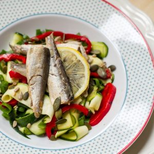 sardines on zucchini ribbons and red peppers with lemon in patterned white bowl