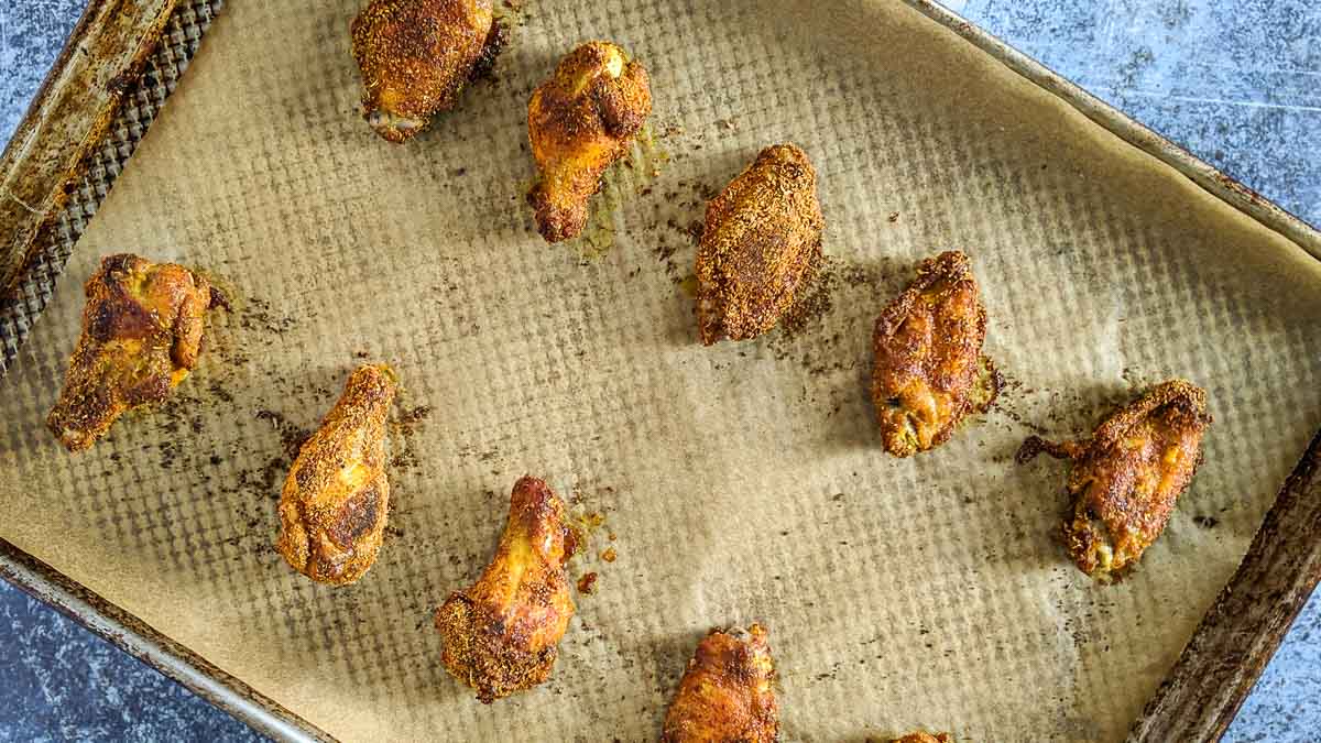 Golden brown chicken wings rest on a parchment-lined baking sheet, evenly spaced to ensure perfect crispiness.