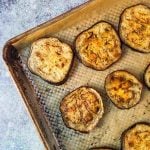 Baked eggplant slices rest elegantly on a baking sheet lined with parchment paper, perfectly roasted to perfection.