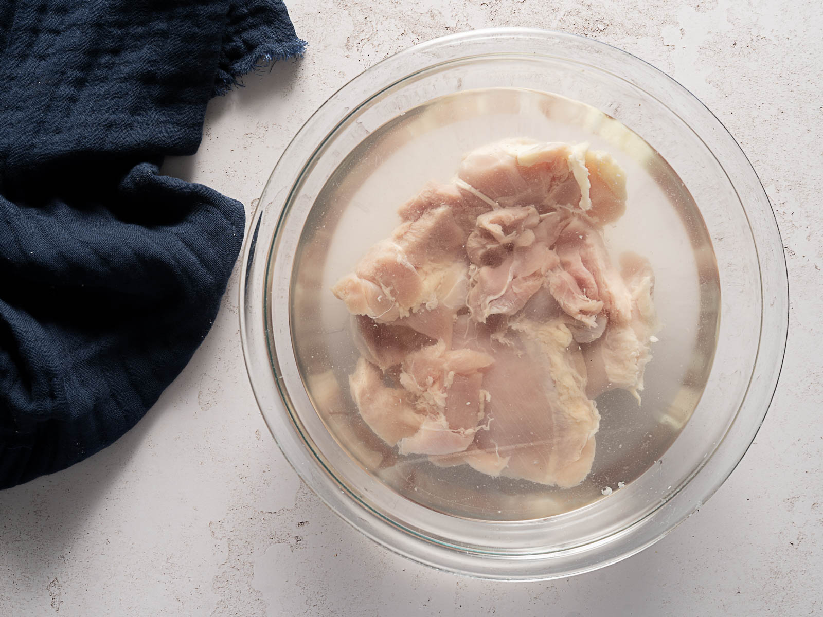 Raw chicken pieces soaking in a glass bowl filled a simple salt brine.