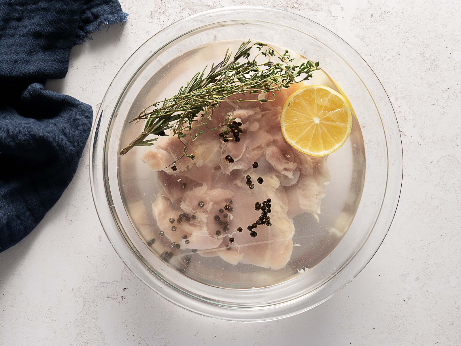Raw chicken pieces in a glass bowl with seasoned brine.