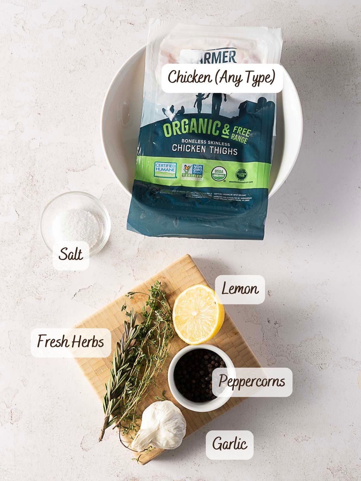 Raw chicken thighs, salt, fresh herbs, lemon, peppercorns, and garlic arranged on a countertop-perfect ingredients if you're learning how to brine chicken for extra flavor before cooking.