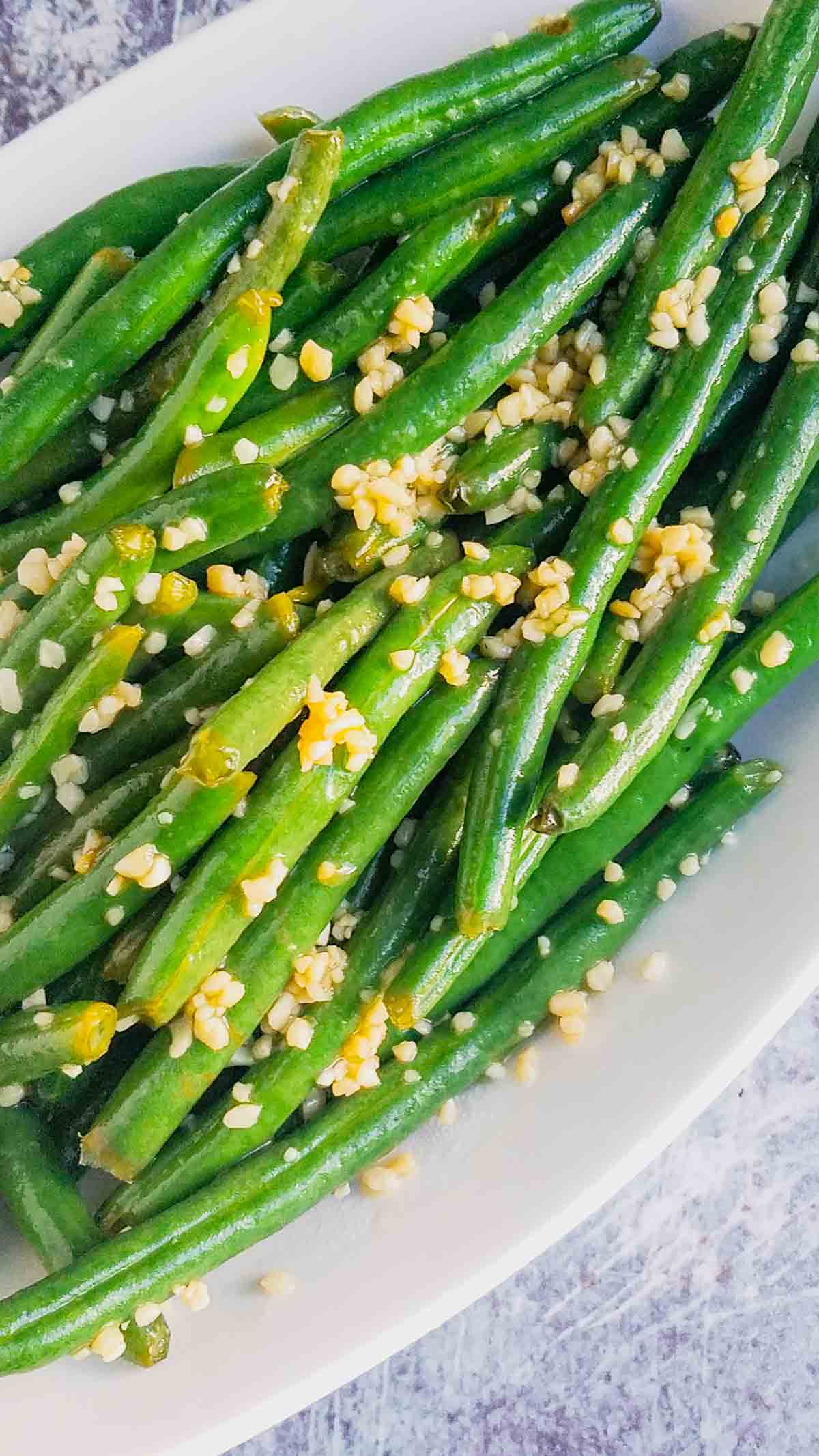A white dish filled with garlic green beans, perfectly cooked and topped with freshly chopped garlic.