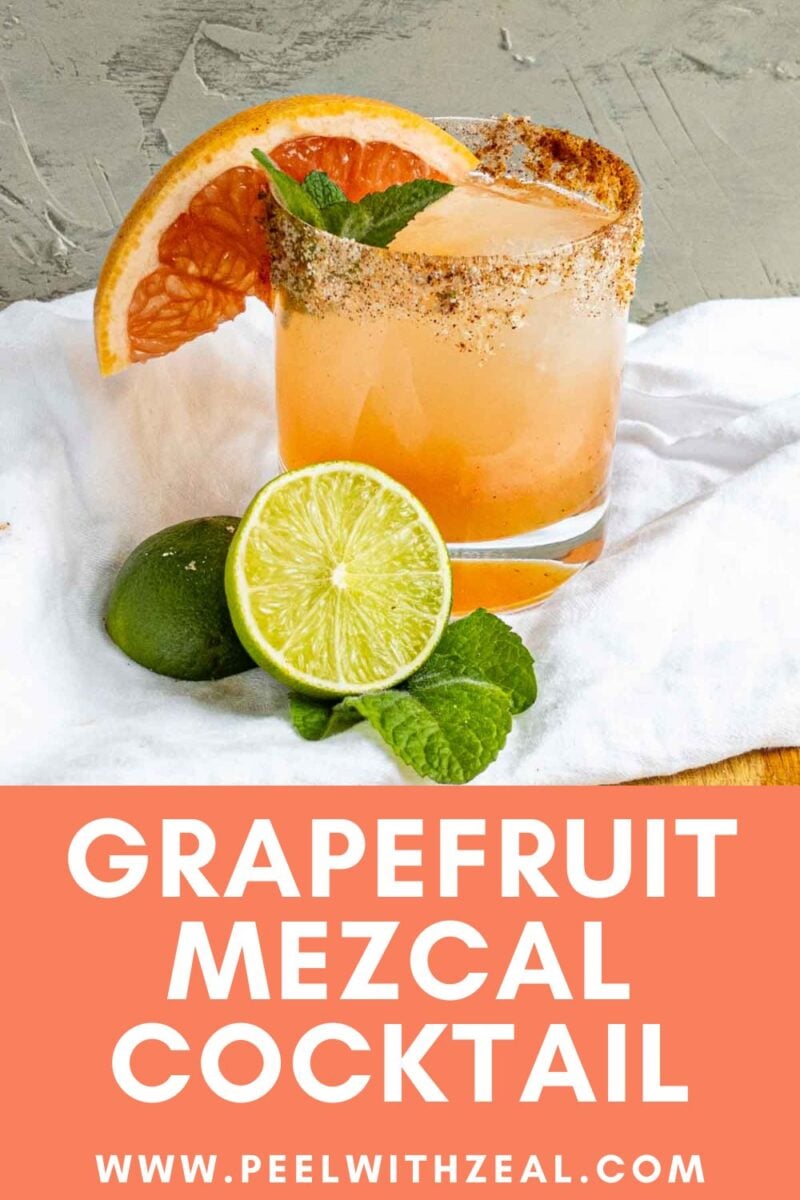 A mezcal paloma cocktail in a glass with a spiced rim, garnished with a grapefruit slice and mint. A halved lime and mint leaves rest beside the glass on a white cloth. Text below reads "GRAPEFRUIT MEZCAL COCKTAIL www.peelwithzeal.com".