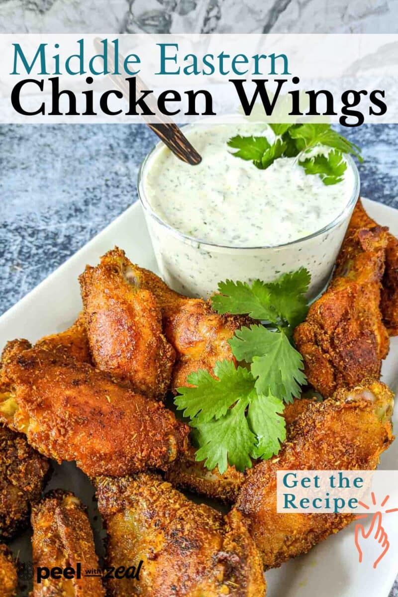 Crispy chicken wings on a plate with a bowl of creamy dip, garnished with cilantro, make the perfect appetizer against a marble background.
