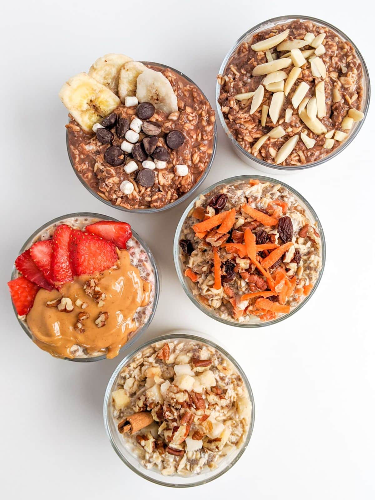 Five bowls of overnight oats with various toppings: bananas and chocolate chips, almonds, peanut butter and strawberries, carrots and raisins, and a nut mix.