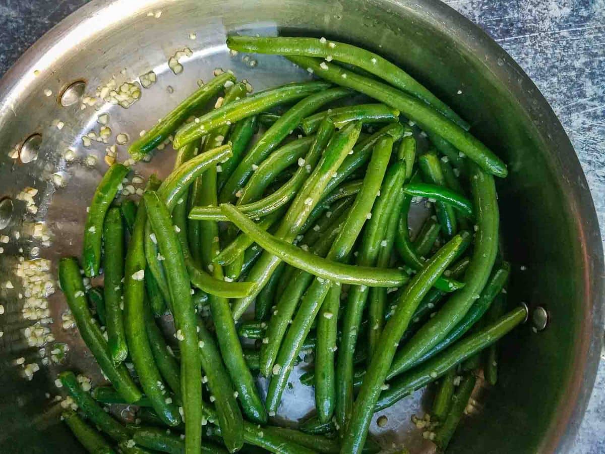 Garlic green beans sautéed in a stainless steel pan, served on a rustic dark surface.