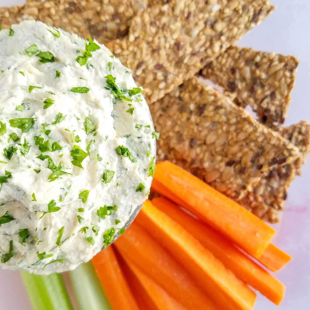 herb and garlic vegan cheese in a bowl with celery and carrots