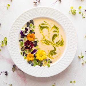 chilled peach soup in white bowl with microgreens