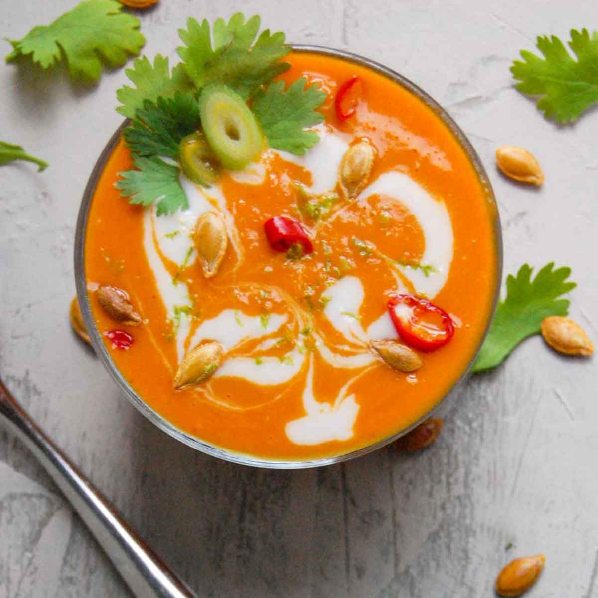 Small bowl of pumpkin soup with fresh cilantro in a cup.