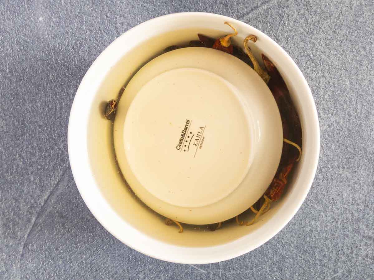 dried chilis soaking in a bowl with a plate holding them down