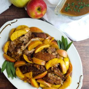 Braised pork shoulder with sages and apples on a platter gravy boat to side.