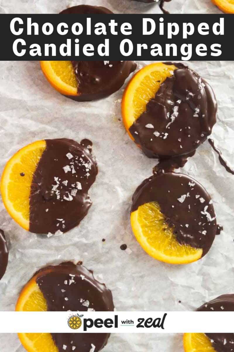 Candied orange slices partially dipped in chocolate and sprinkled with sea salt, arranged on a sheet of parchment paper.