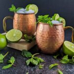 two mezcal mule cocktails in copper mugs with limes and mint