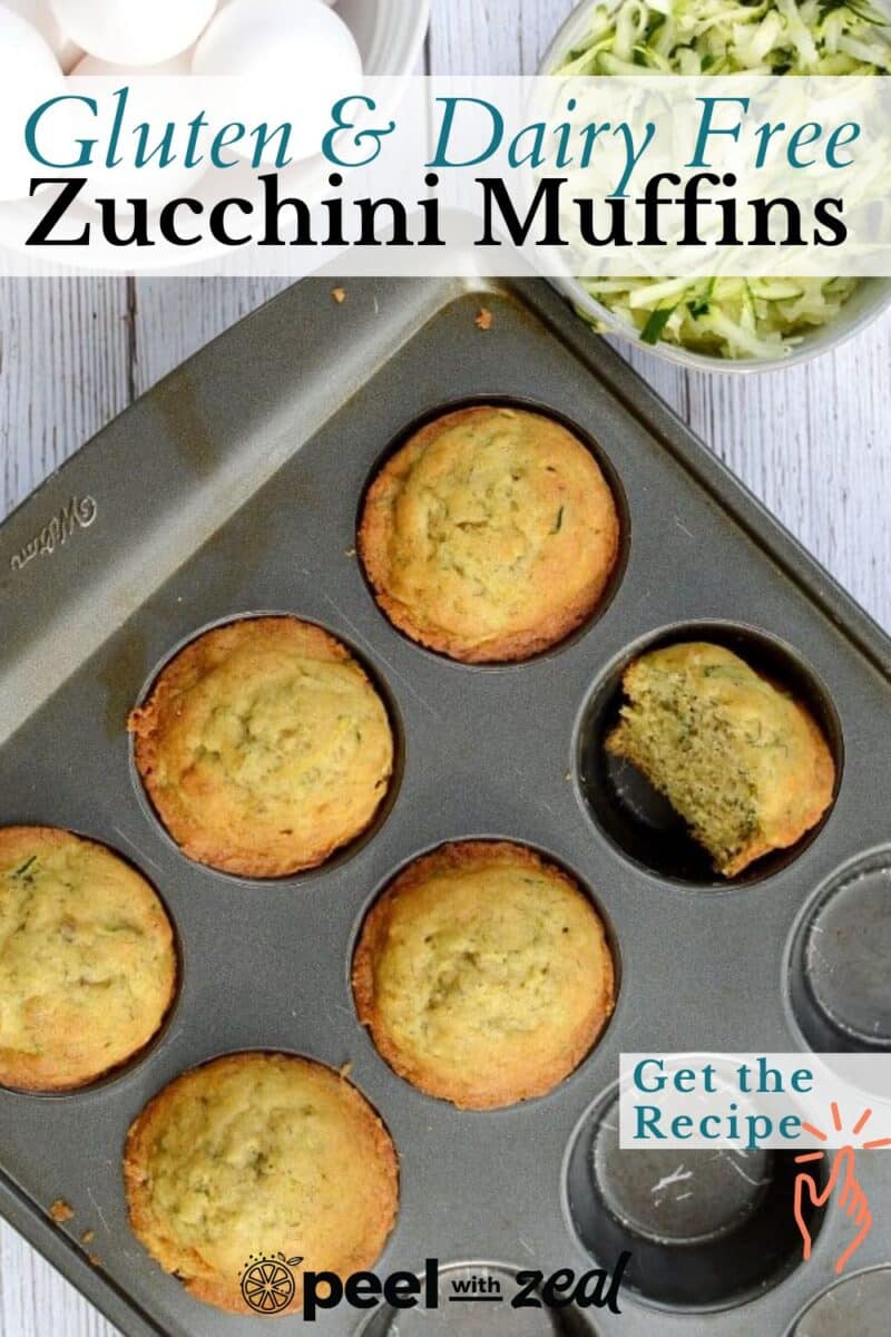 A muffin tray holding six delicious gluten-free zucchini muffins, one enticingly bitten, sits beside a bowl of fresh zucchini shreds. Text: "Gluten & Dairy Free Zucchini Muffins, Get the Recipe.