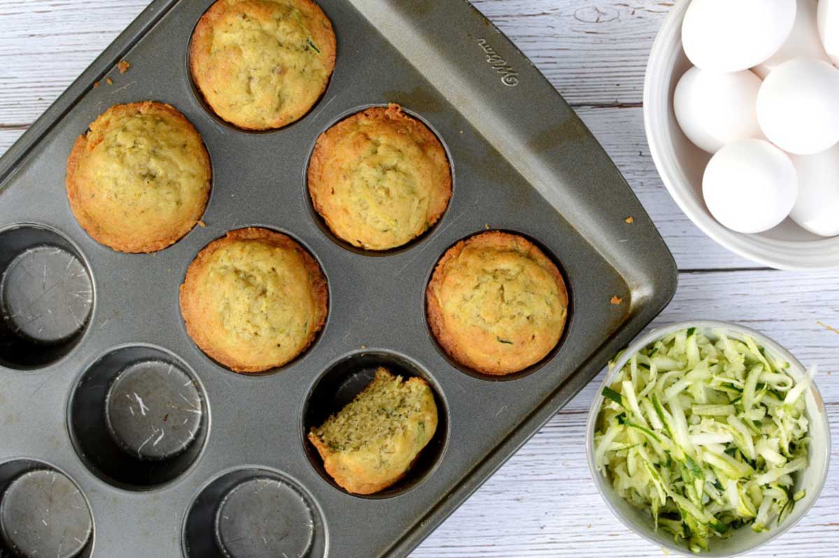 gluten free zucchini muffins in a tin bowl eggs to the side