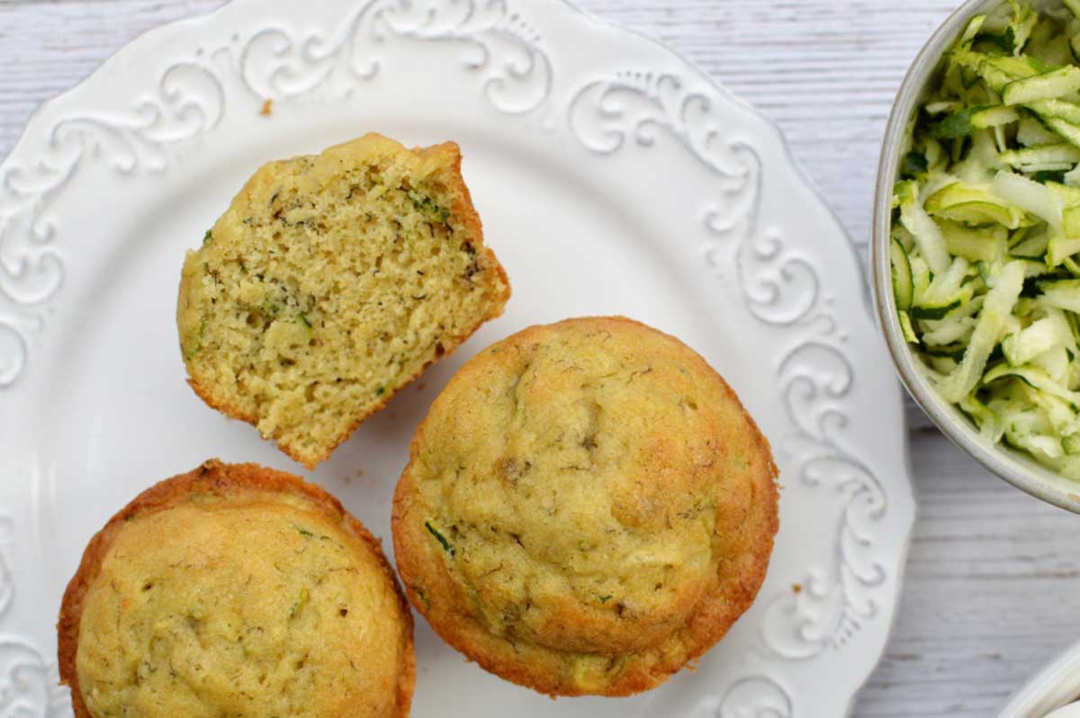 zucchini muffins on a plate and a bowl of grated zucchini