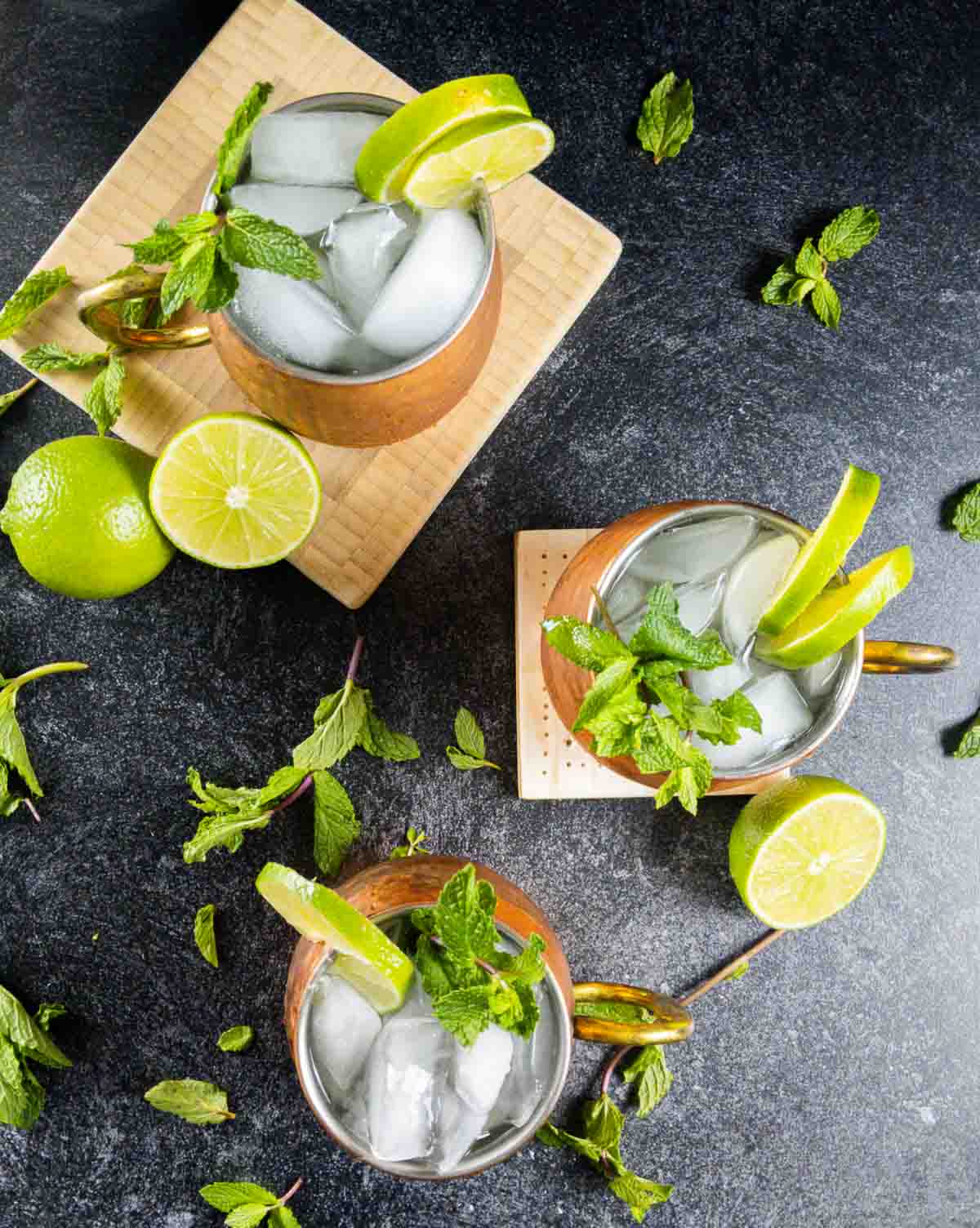 overhead shot of three mezcal mule cocktails in copper mugs on black countertop