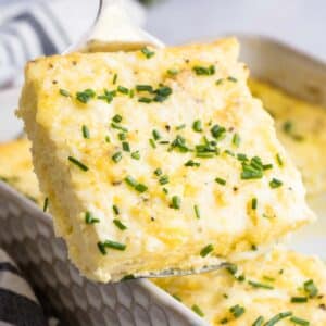 A slice of gluten free breakfast casserole topped with chopped chives is lifted from a baking dish.