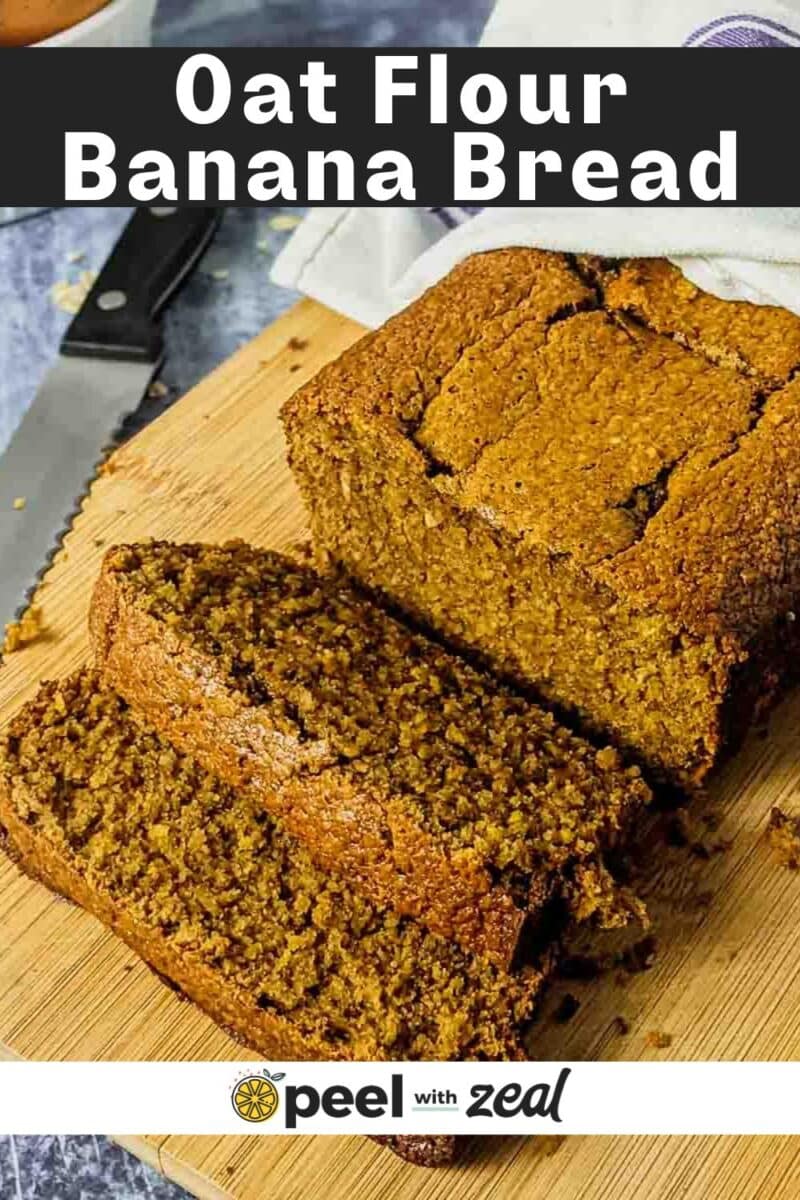 A loaf of Oat Flour Banana Bread rests on a wooden cutting board, with one slice cut and a bread knife beside it.