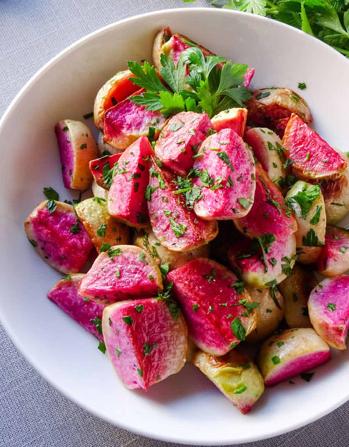 Roasted Watermelon Radishes are the perfect vegan winter recipe. Simple prep, bright flavors and a color scheme that is a feast for the eyes. We love this recipe! Peelwithzeal.com Cooked watermelon radishes in a white bowl with parsley.