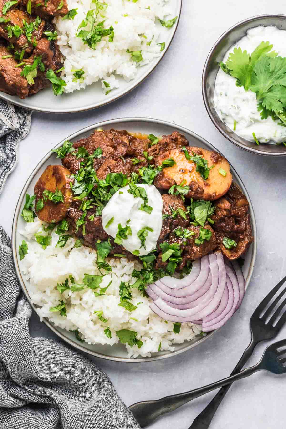 Plates of lamb vindaloo on table with a side of raita.