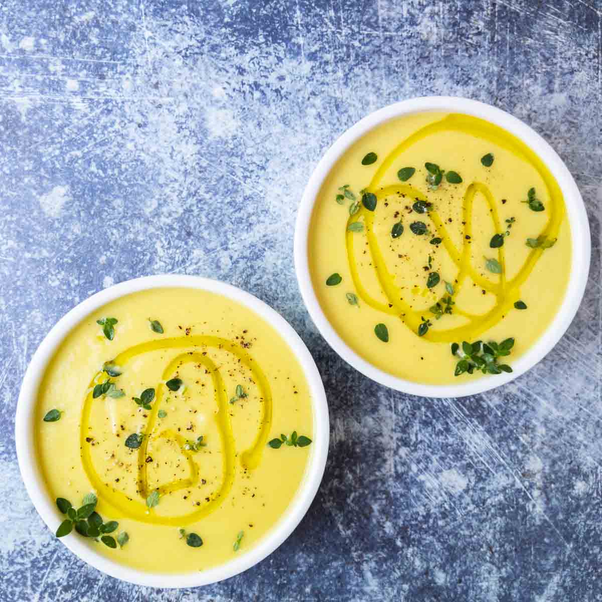 two bowls of creamy yellow squash soup on a blue background